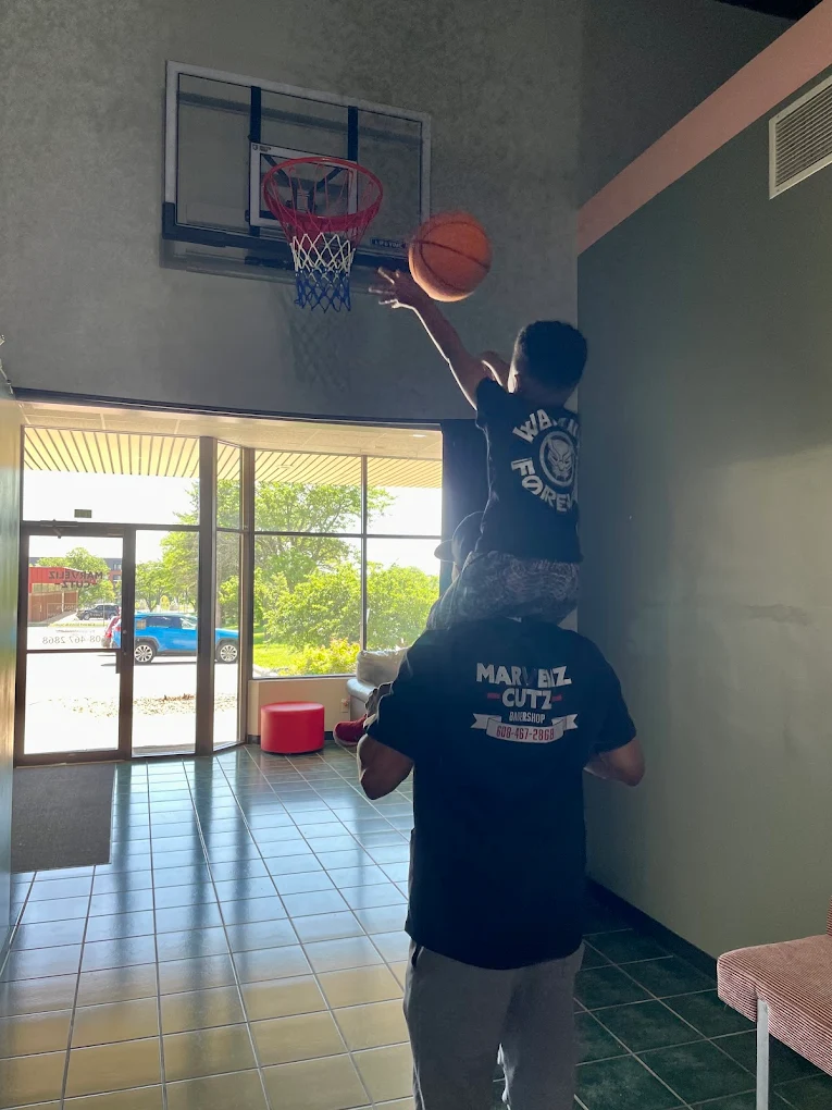 Ron lifting a young community member to the basketball hoop inside Marveliz Cutz